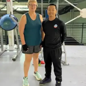Personal trainer standing with older female client inside fitness center.