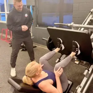 Personal trainer coaching woman on leg press machine.