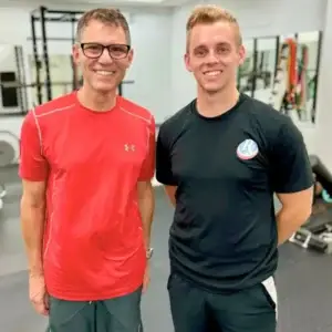 Personal trainer standing with male client inside training facility.