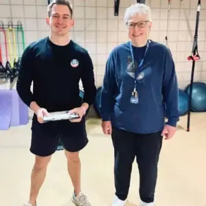 Personal trainer holding clipboard standing next to older female client.