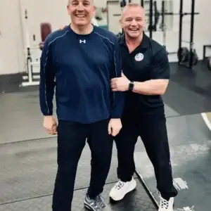 Personal trainer standing with male client inside a strength training gym.