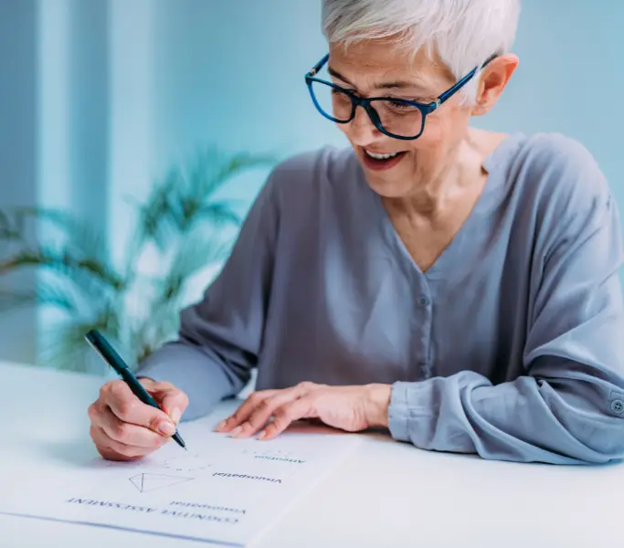 Older woman with glasses reviewing paperwork at a desk, focused and mentally engaged.