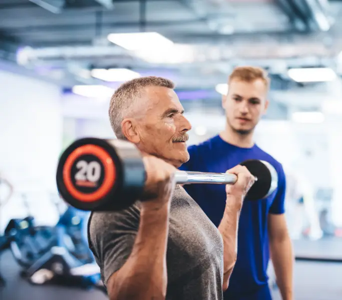 Older man lifting weights with trainer, representing strength and lean muscle maintenance.
